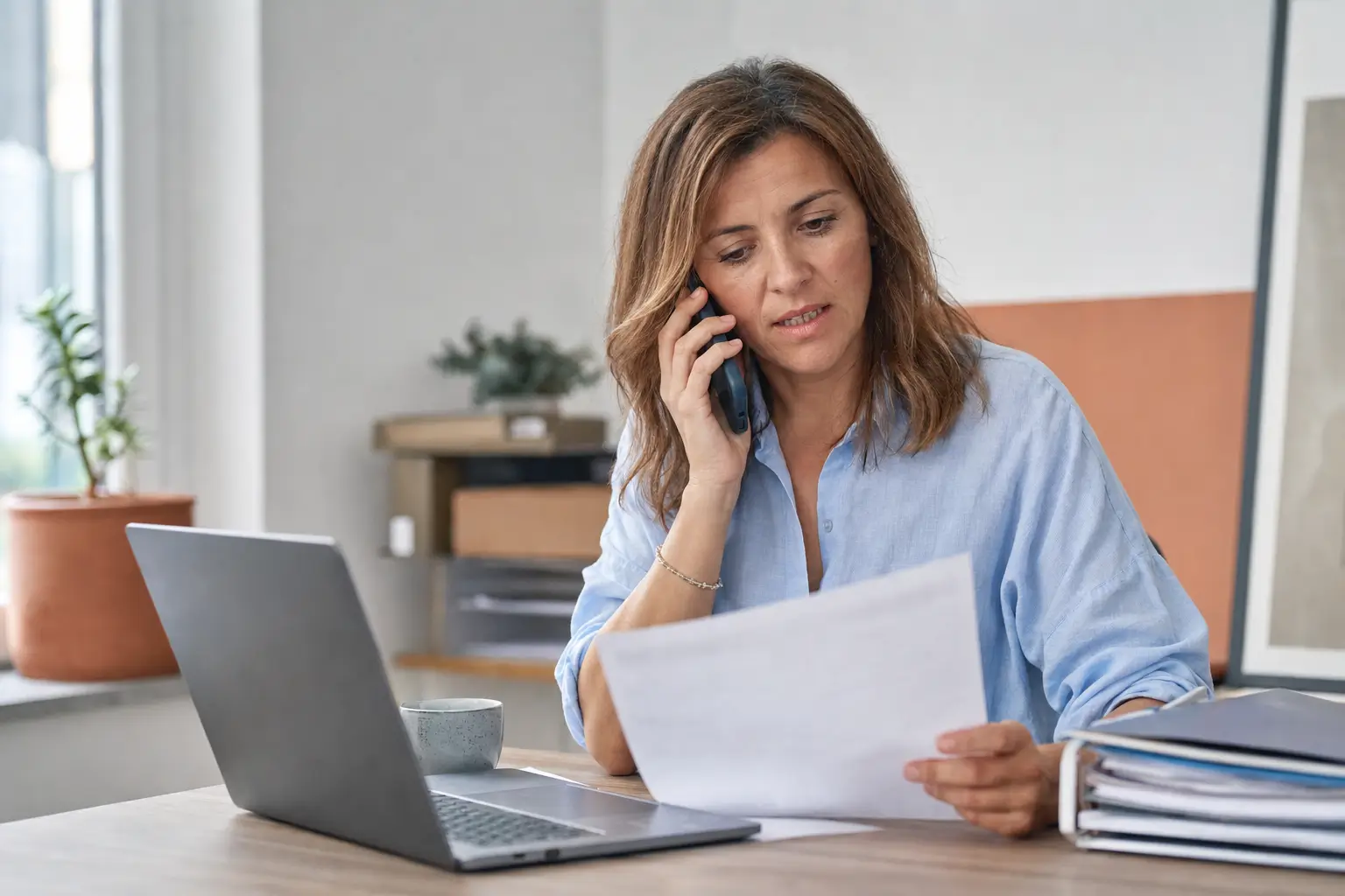 Une dirigeante de petite entreprise au téléphone avec son conseiller OPCO, un bulletin de paie à la main pour y relever son code IDCC